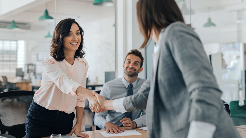 Two women shaking hands at an office desk